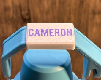 May include: A light blue water bottle with a white label that says "CAMERON" in purple lettering.