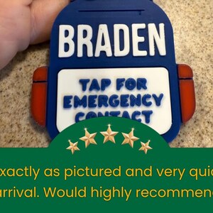 May include: A blue backpack-shaped tag with the name "BRADEN" in white block letters. Below, it reads "TAP FOR EMERGENCY CONTACT." Red accents and gold star graphics are also visible.