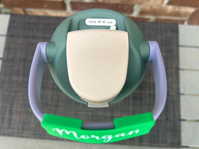 Op de afbeelding: Een groene en beige tuitbeker met een groene handgreep en de naam "Morgan" in het wit. De beker heeft een wit deksel met de labels "Unlock" en "Lock". De handgreep is paars en groen.