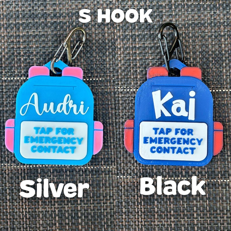 May include: Two blue backpack-shaped keychains with pink and red accents. One keychain says "Audri" and the other says "Kai". Both have the text "TAP FOR EMERGENCY CONTACT". One has a silver hook, the other a black hook.