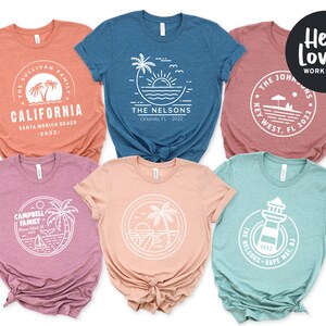 May include: Set of six t-shirts with different designs featuring a beach theme. Each shirt has a white circle with a design inside and text below. The text includes the family name, location, and year. The shirts are in different colors: orange, blue, pink, peach, and teal.