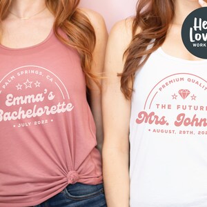 May include: Two white tank tops with pink text. The top on the left says "Palm Springs, CA Emma's Bachelorette July 2022." The top on the right says "Premium Quality The Future Mrs. Johnson August 29th, 2022."