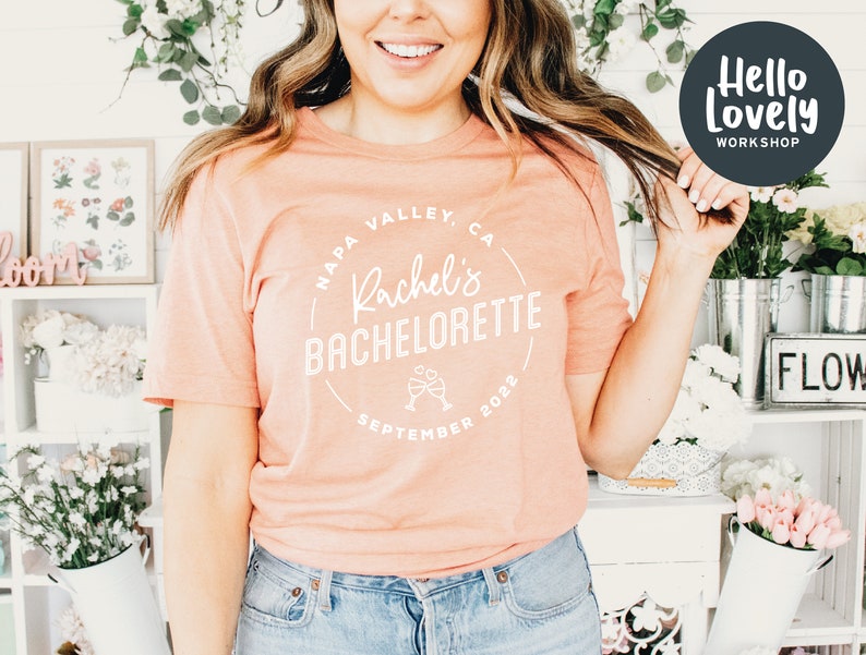 Puede incluir: Una camiseta de color melocot&oacute;n con un gr&aacute;fico circular blanco que dice "Napa Valley, CA Rachel's Bachelorette Septiembre 2022" con un gr&aacute;fico de dos copas de champ&aacute;n.
