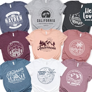 May include: A set of ten t-shirts with various designs featuring family vacation themes. The designs include a cabin in the mountains, a palm tree on a beach, a camper van, and a mountain range. The t-shirts are in various colors, including gray, blue, maroon, and pink.