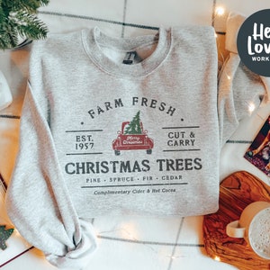 Può includere: Una felpa grigia con un design di fattoria di alberi di Natale in stile vintage. Il design presenta un camion rosso con un albero di Natale in cima, il testo "Farm Fresh", "Est. 1957", "Cut & Carry", "Christmas Trees", "Pine - Spruce - Fir - Cedar" e "Complimentary Cider & Hot Cocoa".