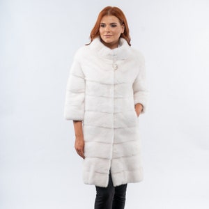 以下が含まれることがあります： 襟が高く、ボタンが1つ付いた白い毛皮のコート。コートは滑らかで絹のような生地で裏打ちされています。