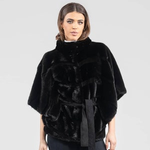 May include: A black fur cape with a suede belt. The cape has a high collar and short sleeves.