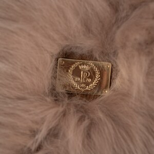 May include: Close-up of a light brown, fluffy material with a rectangular, gold-coloured metal plaque. The plaque features a crown, the letter "P", and the numbers "1970" within a laurel wreath design.