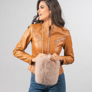 May include: A tan leather jacket with a zip-up front and a small, light pink fluffy purse with a gold chain strap. The jacket has a classic biker style with a stand-up collar and zippered pockets.
