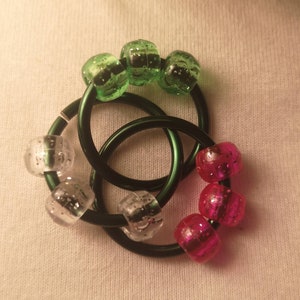 May include: A set of three interlocking rings with green, pink and clear beads. The rings are made of metal and the beads are plastic.