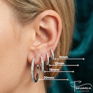 May include: An ear displaying four silver hoop earrings of varying sizes, each adorned with small, clear stones. The sizes are 8mm, 12mm, 16mm, and 20mm. The brand name "Tooriano London" is visible. The background is a dark teal color.