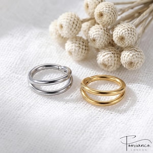 May include: Two double-banded hoop rings, one in a polished silver tone and one in a gold tone, positioned side by side. The rings feature a smooth, rounded metal construction with a continuous circular design, presented clearly for viewing.