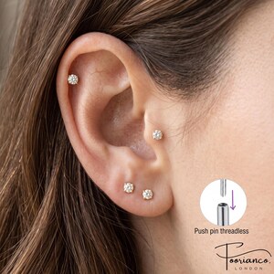 May include: Four small gold-tone stud earrings with clear round stones are placed in the ear. A circular inset diagram shows the push pin threadless mechanism with a downward arrow and the text Push pin threadless. The brand name Poorianco London is visible.