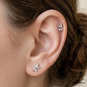May include: A silver-toned ear stud and a matching cartilage earring, both featuring a delicate leaf-shaped design with a small, clear, round-cut stone embedded at the base of the leaves, securely fastened to the ear cartilage and the earlobe.