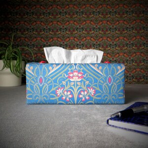 May include: A blue tissue box cover with a floral pattern. The pattern features pink and white flowers with green leaves on a blue background.