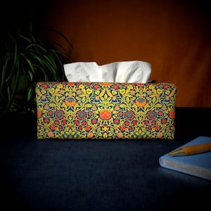 May include: A tissue box cover with a floral pattern in shades of yellow, red, and blue. The pattern features stylised flowers and leaves on a dark blue background.