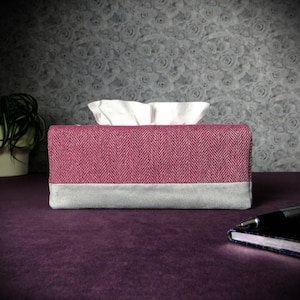 May include: A pink and grey tissue box cover with a herringbone pattern. The cover is made of fabric and has a grey bottom.