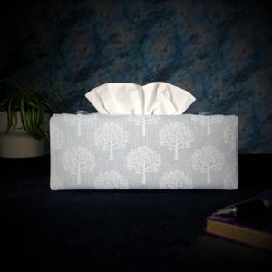 May include: A light blue tissue box cover with a white tree pattern. The cover is made of fabric and has a clear plastic opening for the tissues.