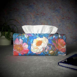May include: A blue tissue box cover with a stained glass design featuring colourful flowers. The flowers are pink, white, and orange with green leaves.