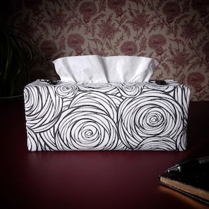 May include: White tissue box cover with a black and white swirl pattern. The cover is made of fabric and has a rectangular shape.
