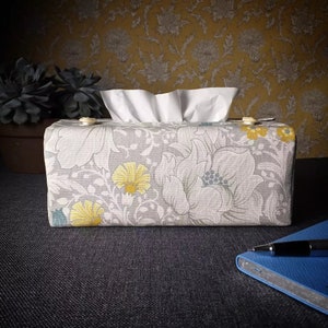 May include: A grey and white floral tissue box cover with yellow flowers. The cover is made of fabric and has a white tissue box inside.