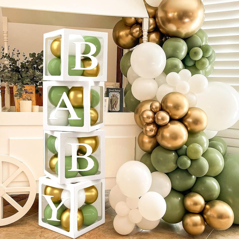 May include: A white box with the letters 'BABY' spelled out in white letters on a green and gold balloon backdrop. The boxes are stacked on top of each other.