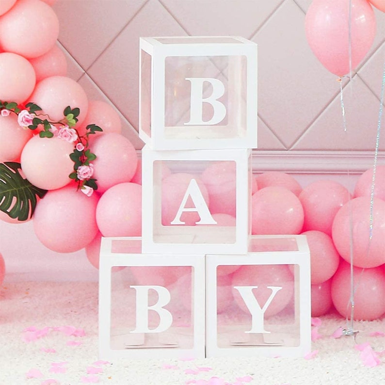 May include: Four clear acrylic boxes with white frames spelling out the word "BABY". The boxes are stacked on top of each other. The boxes are surrounded by pink balloons.