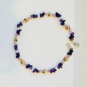 Könnte beinhalten: Ein violettes, rosa und goldenes Perlen-Fußkettchen mit einem silbernen Verschluss. Das Fußkettchen besteht aus kleinen, unregelmäßig geformten Steinen und goldenen Schmetterlingsanhängern.