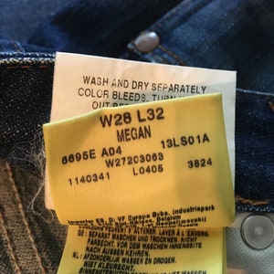 May include: A yellow tag with black text and numbers. The tag reads "Wash and dry separately. Color bleeds. Turn out", "W28 L32 Megan", "6695E A04 W27203063 13LS01A 1140341 L0406 3824", and "Importer ES. D: VF Europe Bybe, Industriepark 5100 Sint-Niklaas, Belgium", "Separat waschen und trocknen. Nicht farbecht, vor dem waschen innenseite nach aussen kehren."