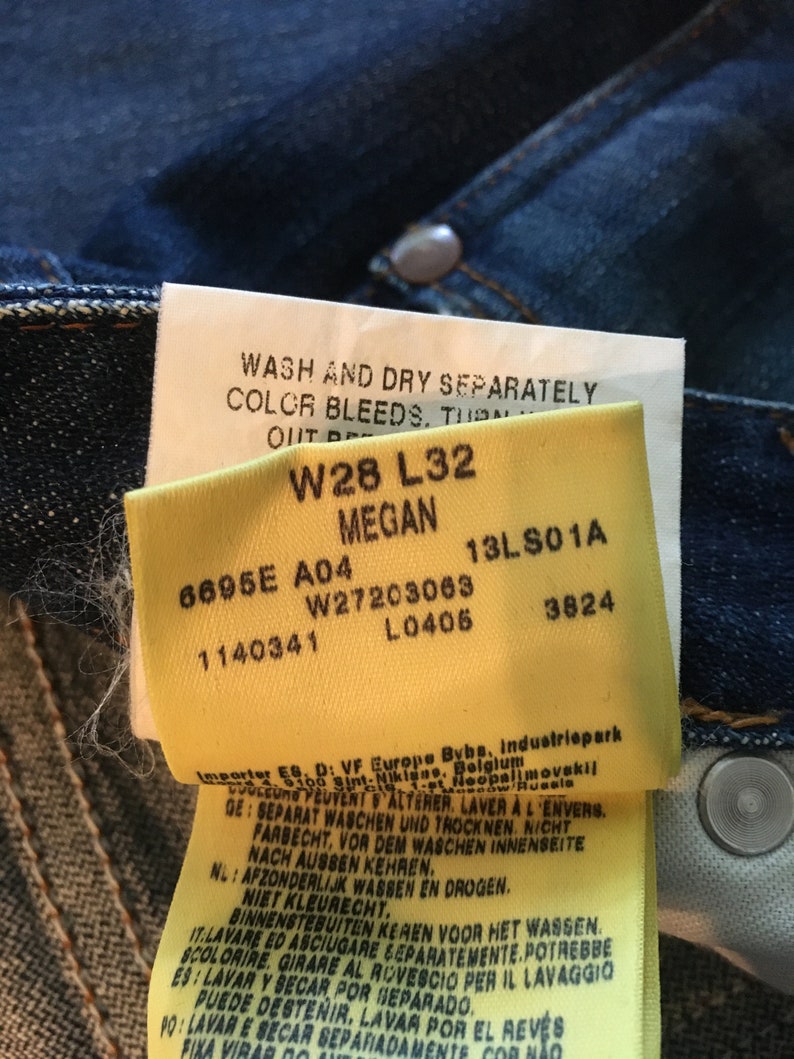 May include: A yellow tag with black text and numbers. The tag reads "Wash and dry separately. Color bleeds. Turn out", "W28 L32 Megan", "6695E A04 W27203063 13LS01A 1140341 L0406 3824", and "Importer ES. D: VF Europe Bybe, Industriepark 5100 Sint-Niklaas, Belgium", "Separat waschen und trocknen. Nicht farbecht, vor dem waschen innenseite nach aussen kehren."