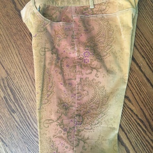 May include: A pair of brown corduroy pants with a paisley print in shades of gold, pink, and purple.
