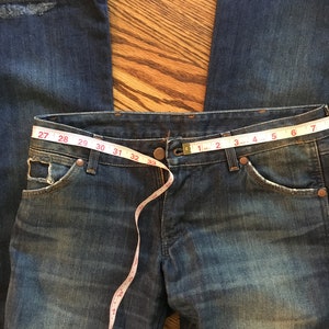 May include: A pair of blue denim jeans with a measuring tape around the waist. The tape reads 27 to 42 inches.