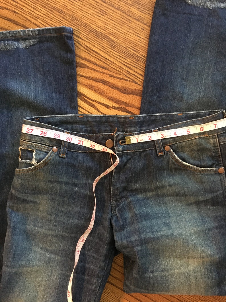 May include: A pair of blue denim jeans with a measuring tape around the waist. The tape reads 27 to 42 inches.