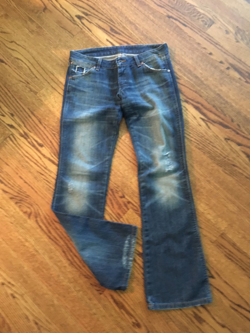 May include: A pair of blue denim jeans with faded and distressed details. The jeans have a bootcut style and are made of a soft, comfortable fabric.