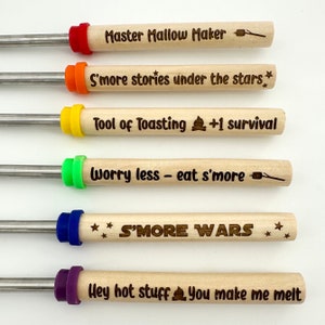 Puede incluir: Seis pinchos de madera con mangos de colores y lemas grabados. Los lemas son: "Master Mallow Maker", "S'more stories under the stars", "Tool of Toasting +1 survival", "Worry less - eat s'more", "S'MORE WARS" y "Hey hot stuff You make me melt".