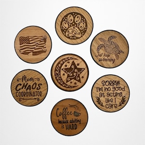 May include: Set of 7 round wooden coasters with various designs and sayings. The designs include a paw print, a turtle, a crescent moon and star, an American flag, a coffee cup, and two sayings. The sayings are "Mom Chaos Coordinator", "Just keep swimming", "Coffee because adulting is hard", and "Sorry! I'm no good at acting like I care".