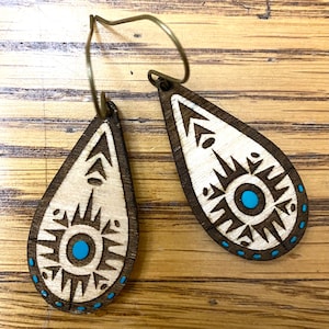May include: A pair of wooden teardrop-shaped earrings with a geometric design and turquoise accents.