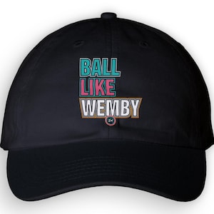 Könnte beinhalten: Eine schwarze Baseballkappe mit dem aufgedruckten Text BALL LIKE WEMBY auf der Vorderseite. Das Wort BALL ist in Türkis, LIKE in Pink und WEMBY in Weiß mit orangefarbenem Umriss gehalten. Unter dem Text befindet sich ein kleines Logo mit SA.