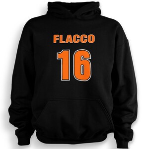Puede incluir: Sudadera con capucha negra con el nombre "FLACCO" en letras naranjas en bloque sobre el número "16" en naranja con contorno blanco. La sudadera tiene un bolsillo delantero y una capucha con cordón.