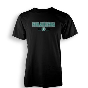 Puede incluir: Camiseta negra con un gráfico verde y blanco que dice "PHILADELPHIA" con una "P" verde en un círculo.
