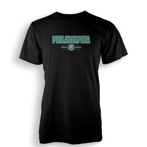 Puede incluir: Camiseta negra con un gráfico verde y blanco que dice "PHILADELPHIA" con una "P" verde en un círculo.