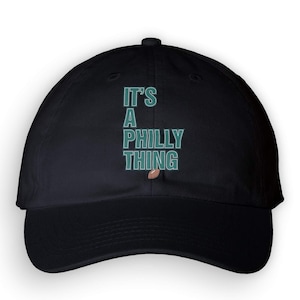 May include: Black baseball cap with the text "IT'S A PHILLY THING" in teal and white. A brown football graphic is below the text. The cap is a classic, unstructured style.