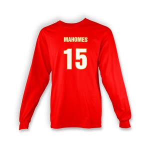 Op de afbeelding: Rood T-shirt met lange mouwen met de naam "Mahomes" en het nummer "15" gedrukt in wit met een gele omtrek.