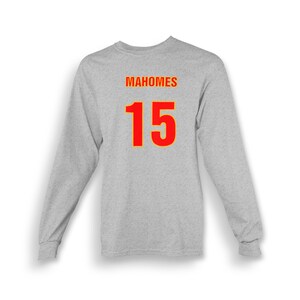 Op de afbeelding: Een grijs longsleeve t-shirt met de naam "MAHOMES" en het nummer "15" gedrukt op de rug in rood met een gele omtrek.