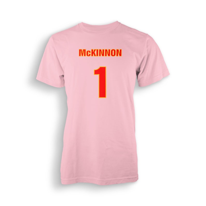 以下が含まれることがあります： ピンクのTシャツに「MCKINNON」という名前と「1」という数字が、黄色の輪郭で囲まれた赤色で印刷されています。