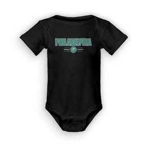 Puede incluir: Mono negro para bebé con un gráfico verde y blanco que dice "PHILADELPHIA" con un logotipo verde y blanco debajo.
