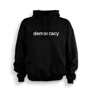 Könnte beinhalten: Schwarzer Kapuzenpullover mit dem Wort "Demokratie" in weiß auf der Vorderseite.