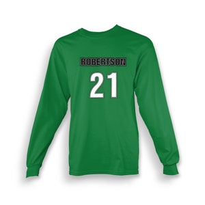 Może przedstawiać: Zielony T-shirt z długim rękawem z nadrukiem imienia "ROBERTSON" i numeru "21" na przodzie w kolorze czarnym i białym.