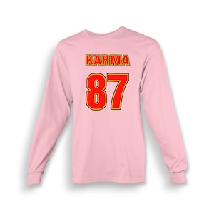 Op de afbeelding: Roze longsleeve t-shirt met het woord "KARMA" en het nummer "87" gedrukt op de achterkant in rood met een gele omtrek.