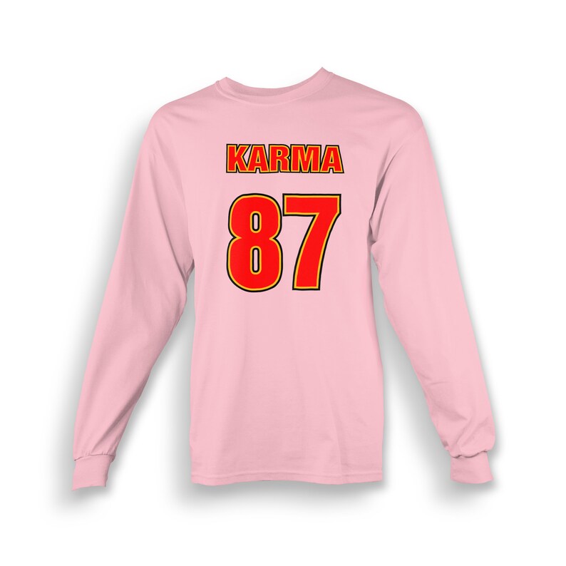 Op de afbeelding: Roze longsleeve t-shirt met het woord "KARMA" en het nummer "87" gedrukt op de achterkant in rood met een gele omtrek.